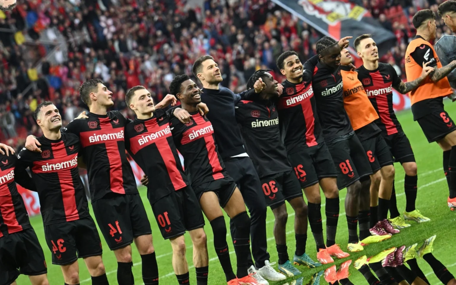 O que explica o sucesso do Bayer Leverkusen na temporada? Elenco do Bayer Leverkusen comemora mais uma vitória com a sua torcida (Foto: INA FASSBENDER / AFP)